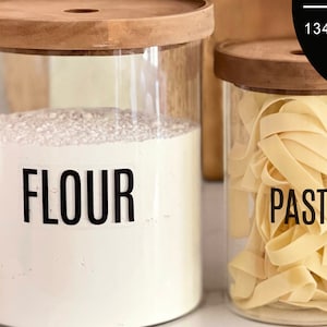 May include: Three glass jars with wooden lids and black labels. The labels read "Flour", "Pasta", and "Baking Powder".