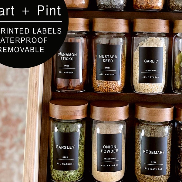 Puede incluir: Un juego de tarros de especias de vidrio con tapas de madera y etiquetas negras. Las etiquetas tienen texto blanco que dice "Canela en rama", "Semilla de mostaza", "Ajo", "Hojas de laurel", "Perejil", "Polvo de cebolla", "Romero" y "Pimienta negra".
