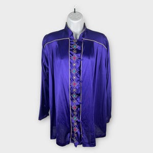 May include: A long-sleeved, purple satin robe with a mandarin collar. The robe features a decorative center panel with colorful embroidered diamond shapes and gold trim. The robe is displayed on a white mannequin.