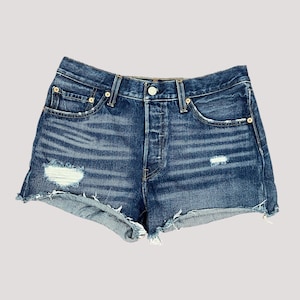 May include: Blue denim shorts with a button fly, distressed details, and frayed edges. The shorts have classic five-pocket styling and a high-waisted fit. The denim is a medium wash with subtle fading.