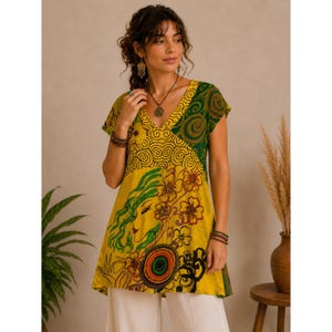 May include: A short-sleeved tunic featuring a vibrant yellow base with a green patterned section on the upper right. The garment displays a graphic print of a stylized face with flowing green hair, floral motifs, and a circular target design.
