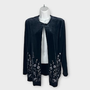 May include: Black velvet jacket with long sleeves and a floral design embroidered in silver thread along the front edges. The jacket has a single button closure at the neckline and is displayed on a mannequin.