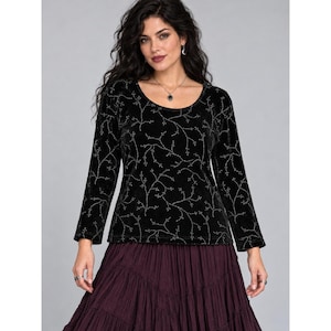 May include: A black long-sleeve top featuring a scoop neckline and a subtle silver embroidered vine pattern throughout the fabric. The garment is paired with a dark purple tiered skirt that has a gathered, flowing texture.