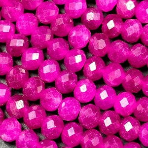 May include: A strand of bright pink faceted gemstone beads. The beads are round and have a smooth, polished finish.