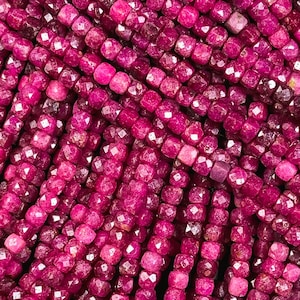 May include: A strand of deep red ruby beads, each bead is faceted and has a square shape.