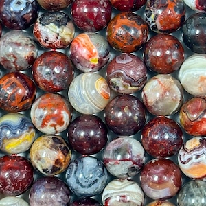 May include: A collection of agate spheres in various shades of red, brown, white, and yellow. The spheres are polished and have intricate patterns of banding and swirls.