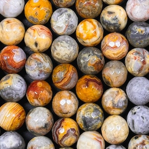 May include: A collection of round, polished agate beads in shades of yellow, brown, and gray. The beads have a natural, marbled pattern.