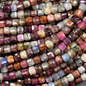 Peut inclure: Un brin de perles de pierres précieuses facettées dans différentes nuances de rouge, bleu et marron. Les perles sont de forme carrée et ont une finition polie.