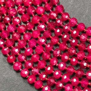 May include: A strand of bright pink faceted gemstone beads. The beads are round and have a smooth, polished finish.