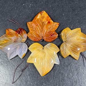 Könnte beinhalten: Vier Agat-Blatt-Anhänger in Orange- und Gelbtönen. Die Blätter sind mit Adern geschnitzt und haben eine transluzente Qualität.