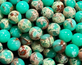 Puede incluir: Una hebra de cuentas redondas marmoleadas de color verde, marrón y blanco. Las cuentas tienen un diámetro aproximado de 8 mm y un acabado liso y pulido.