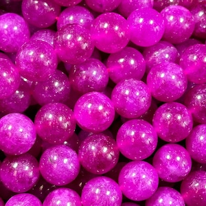 May include: A close-up of a pile of round, bright purple beads. The beads are smooth and shiny, and they have a slightly translucent quality.