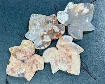 May include: Four agate leaf pendants with brown string attached. The leaves are carved in a detailed ivy leaf shape and have a white, brown, and pink agate pattern.