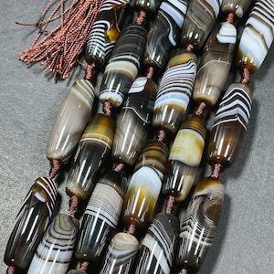 May include: A strand of brown, white, and black banded agate beads. The beads are oval shaped and have a polished finish. The beads are strung on a brown cord.
