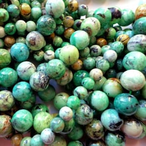 May include: A close-up of a strand of green and brown gemstone beads. The beads are round and have a mottled appearance.