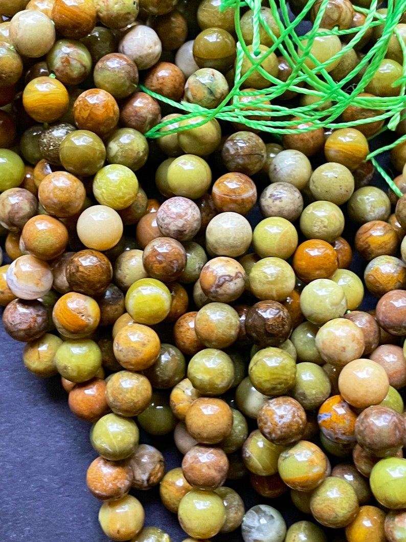 May include: A strand of green, brown, and yellow gemstone beads. The beads are round and have a smooth, polished finish.
