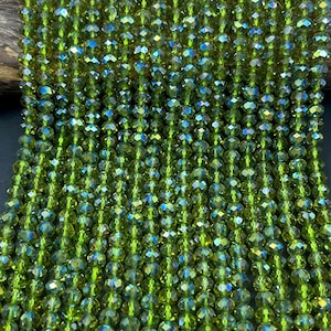 May include: A strand of green faceted glass beads. The beads are small and round, with a slight iridescent sheen.