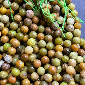 May include: A strand of green opal beads with a variety of brown, green, and yellow tones. The beads are round and smooth, and they are strung on a green thread.