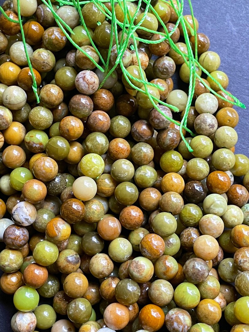 May include: A strand of green opal beads with a variety of brown, green, and yellow tones. The beads are round and smooth, and they are strung on a green thread.
