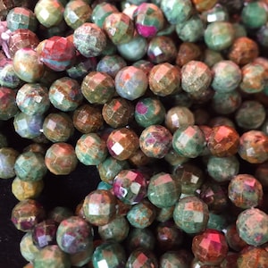 May include: A strand of faceted gemstone beads in shades of green, brown, and red. The beads are irregularly shaped and have a rough, natural texture.