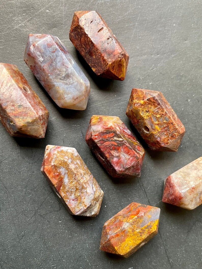 May include: Eight faceted, polished, red, brown, and gold tiger's eye gemstone beads. The beads are all roughly the same size and shape, and they have a smooth, polished finish.