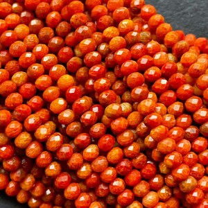 K&ouml;nnte beinhalten: Eine Str&auml;hne orangefarbener Korallenperlen, jede Perle ist facettiert und hat eine leicht unregelm&auml;&szlig;ige Form. Die Perlen sind zu einem Haufen angeordnet, der die Farbe und Textur der Koralle zeigt.