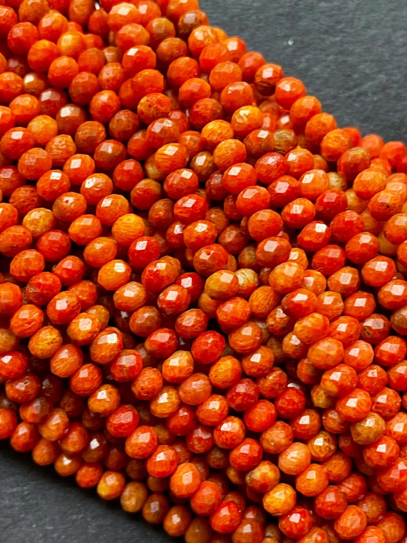 K&ouml;nnte beinhalten: Eine Str&auml;hne orangefarbener Korallenperlen, jede Perle ist facettiert und hat eine leicht unregelm&auml;&szlig;ige Form. Die Perlen sind zu einem Haufen angeordnet, der die Farbe und Textur der Koralle zeigt.
