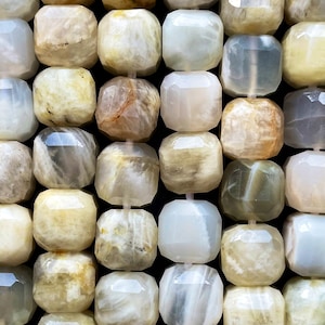 May include: A strand of faceted, iridescent moonstone beads in shades of white, grey, and yellow. The beads are all approximately the same size and shape, and they have a smooth, polished finish.