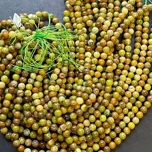 May include: A large pile of green and brown round beads. The beads are made of a natural stone with a mottled pattern.