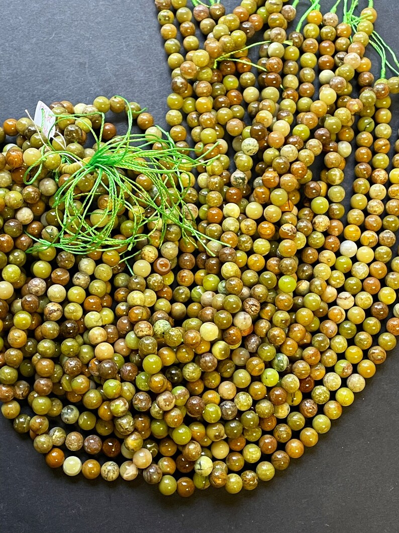 May include: A large pile of green and brown round beads. The beads are made of a natural stone with a mottled pattern.