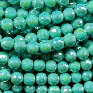 May include: A strand of iridescent teal green faceted glass beads. The beads are round and have a slightly irregular shape.