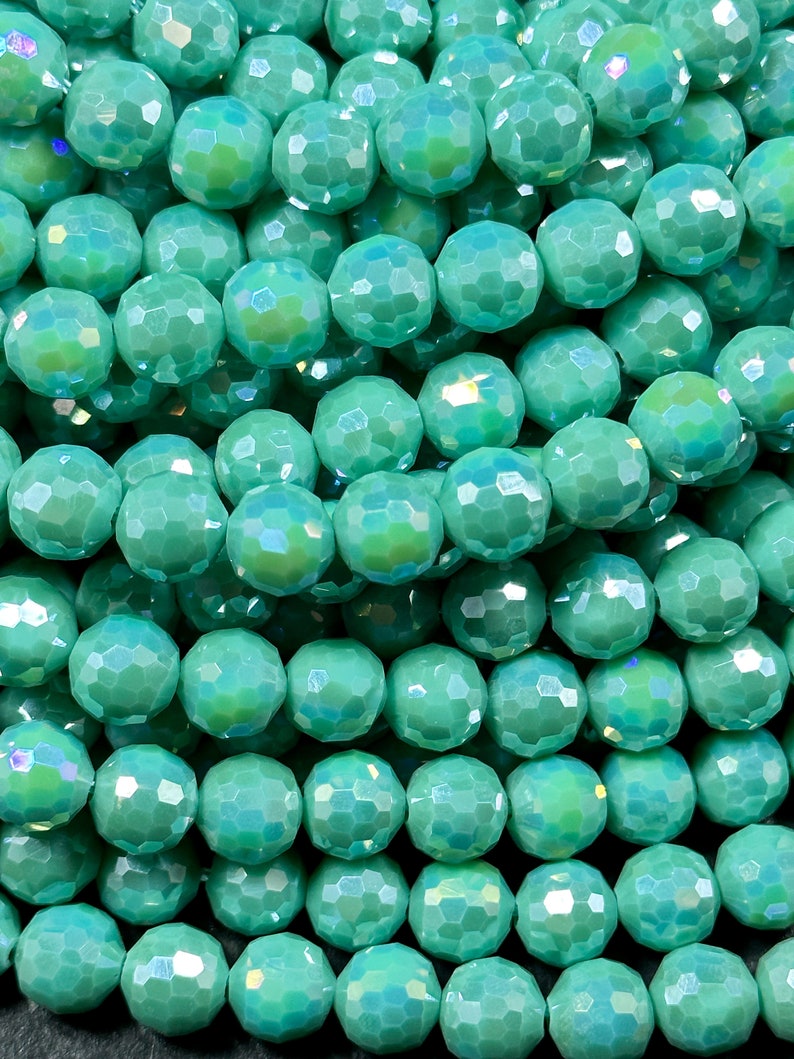 May include: A strand of iridescent teal green faceted glass beads. The beads are round and have a slightly irregular shape.