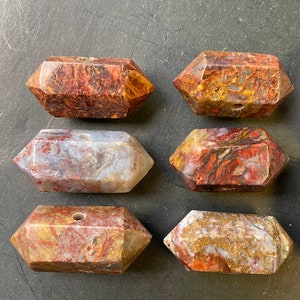 May include: Six red, white and brown agate crystal points with a hole drilled through the centre. The points are arranged in two rows of three.