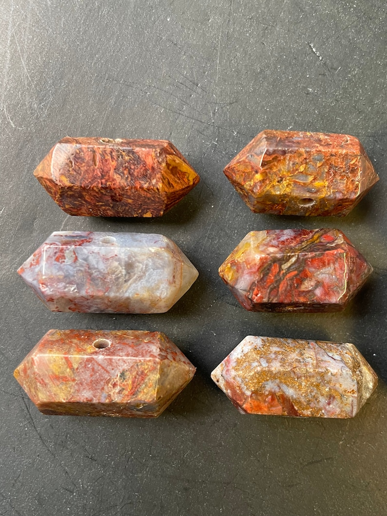 May include: Six red, white and brown agate crystal points with a hole drilled through the centre. The points are arranged in two rows of three.
