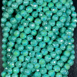 May include: A strand of iridescent teal green faceted glass beads. The beads are round and have a smooth, polished finish.