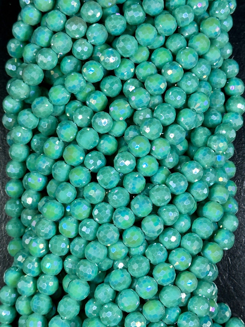 May include: A strand of iridescent teal green faceted glass beads. The beads are round and have a smooth, polished finish.