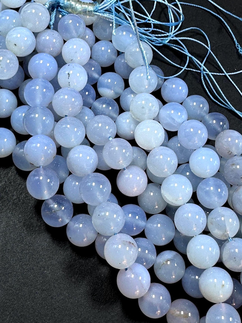Pu&ograve; includere: Una collana di perle di agata blu chiaro, ogni perla &egrave; rotonda e liscia. Le perle sono infilate su un filo blu sottile.