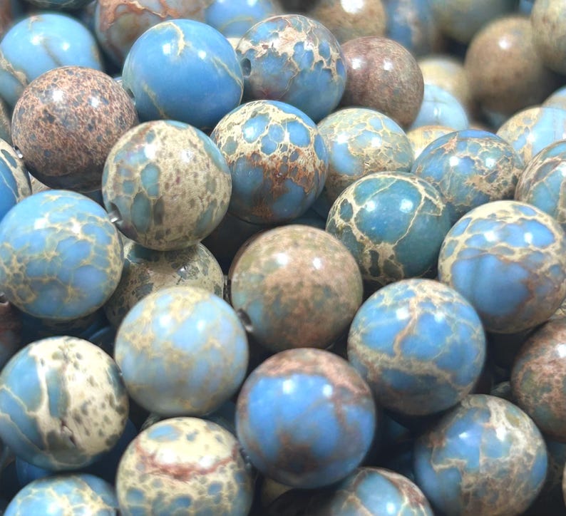 May include: A close-up of a pile of blue and brown jasper beads. The beads are round and have a mottled appearance.