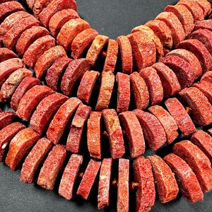 May include: Close-up of a necklace made of red coral beads. The beads are cylindrical and strung together, creating multiple strands. The coral has a textured surface and a natural, organic appearance.