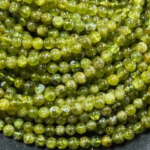 May include: A strand of green gemstone beads. The beads are round and have a slightly translucent appearance. They are all approximately the same size.