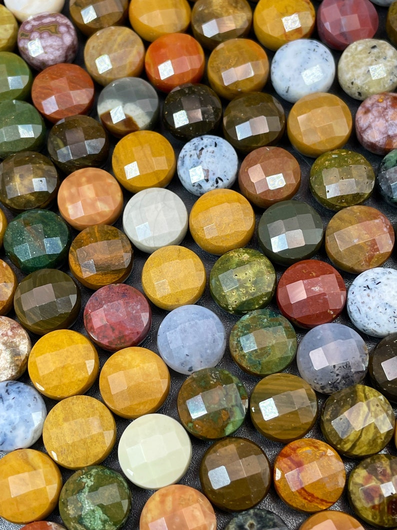 May include: A collection of round, polished gemstone cabochons in various colors and patterns. The stones are arranged in a grid pattern on a gray surface.