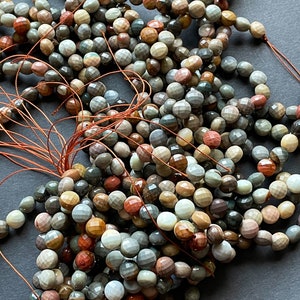 May include: A pile of multi-coloured gemstone beads with a faceted finish. The beads are strung on brown thread and are a mix of brown, red, green, and white.