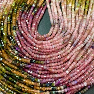 Puede incluir: Una hebra de cuentas de piedras preciosas cuadradas multicolores. Las cuentas son una mezcla de rosa, verde y marrón.