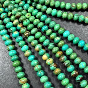 May include: A strand of turquoise beads with a green and brown color variation. The beads are round and have a smooth, polished finish.