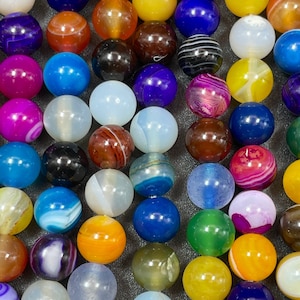 May include: A collection of colorful agate beads with various patterns and colors, including blue, green, yellow, orange, red, and purple. The beads are round and smooth, and they are arranged in rows.