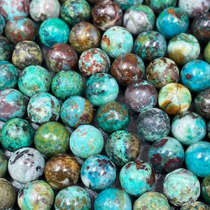 May include: A collection of round, green, brown, and blue gemstone beads. The beads are smooth and polished, with a variety of patterns and textures.