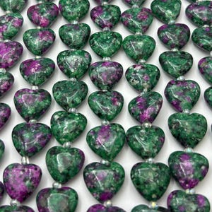 May include: A strand of green and purple heart-shaped beads. The beads are made of a natural stone with a speckled pattern.