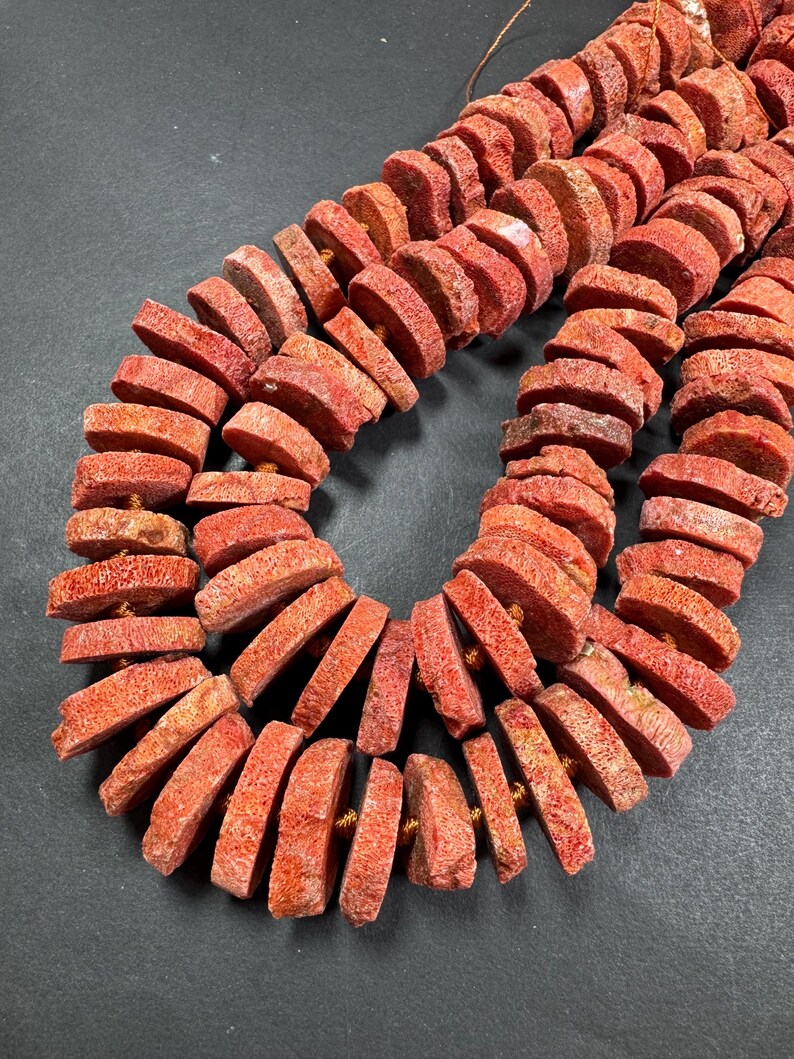 May include: Strands of coral-colored, disc-shaped beads. The beads are strung together, showcasing a natural, textured surface. The color varies from light to deep coral, with visible natural variations. The beads are likely for jewelry making.