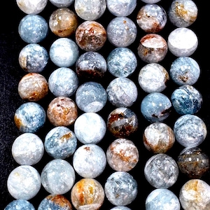 May include: A collection of round, polished gemstones in shades of blue, white, and brown. The stones have a marbled appearance and are arranged closely together against a black background. The gemstones vary in color and pattern.