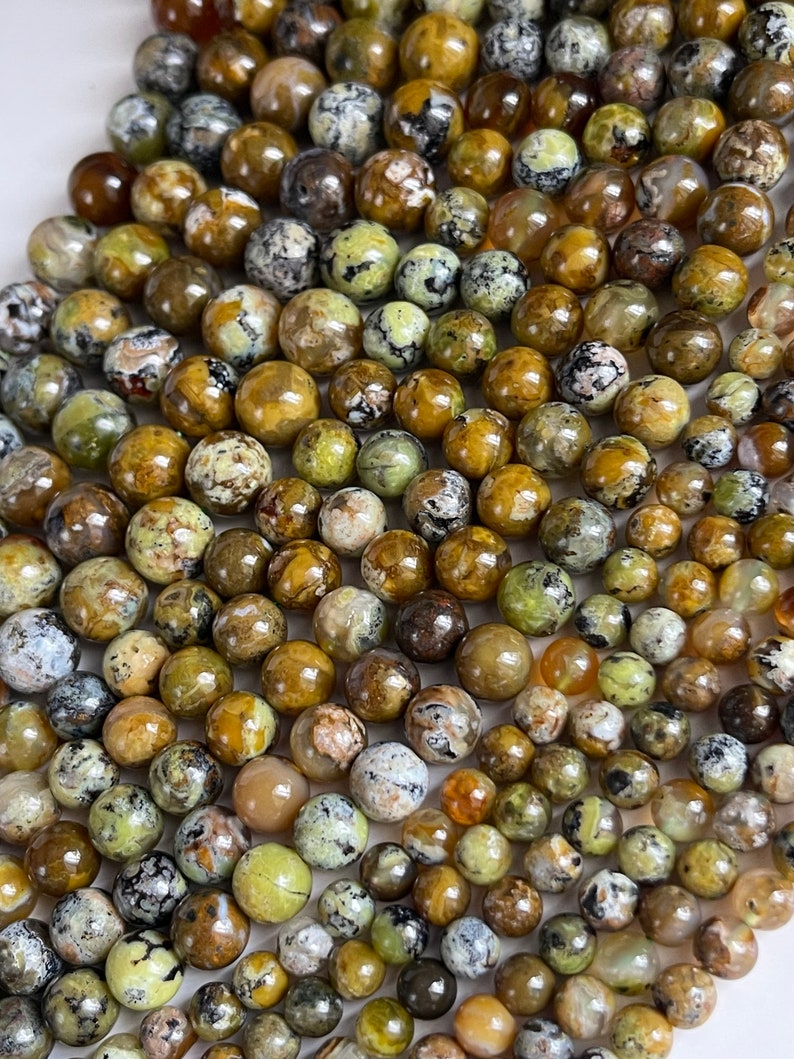 Op de afbeelding: Een streng ronde, groene, bruine en gele opaal kralen. De kralen hebben een gevlekt, gemarmerd uiterlijk.